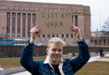 Transpersoner kräver rätt till att vara Alex Oksanen håller upp en skylt med texten "Rätt att vara" ovanför sitt huvud. I bakgrunden syns riksdagshuset i Helsingfors