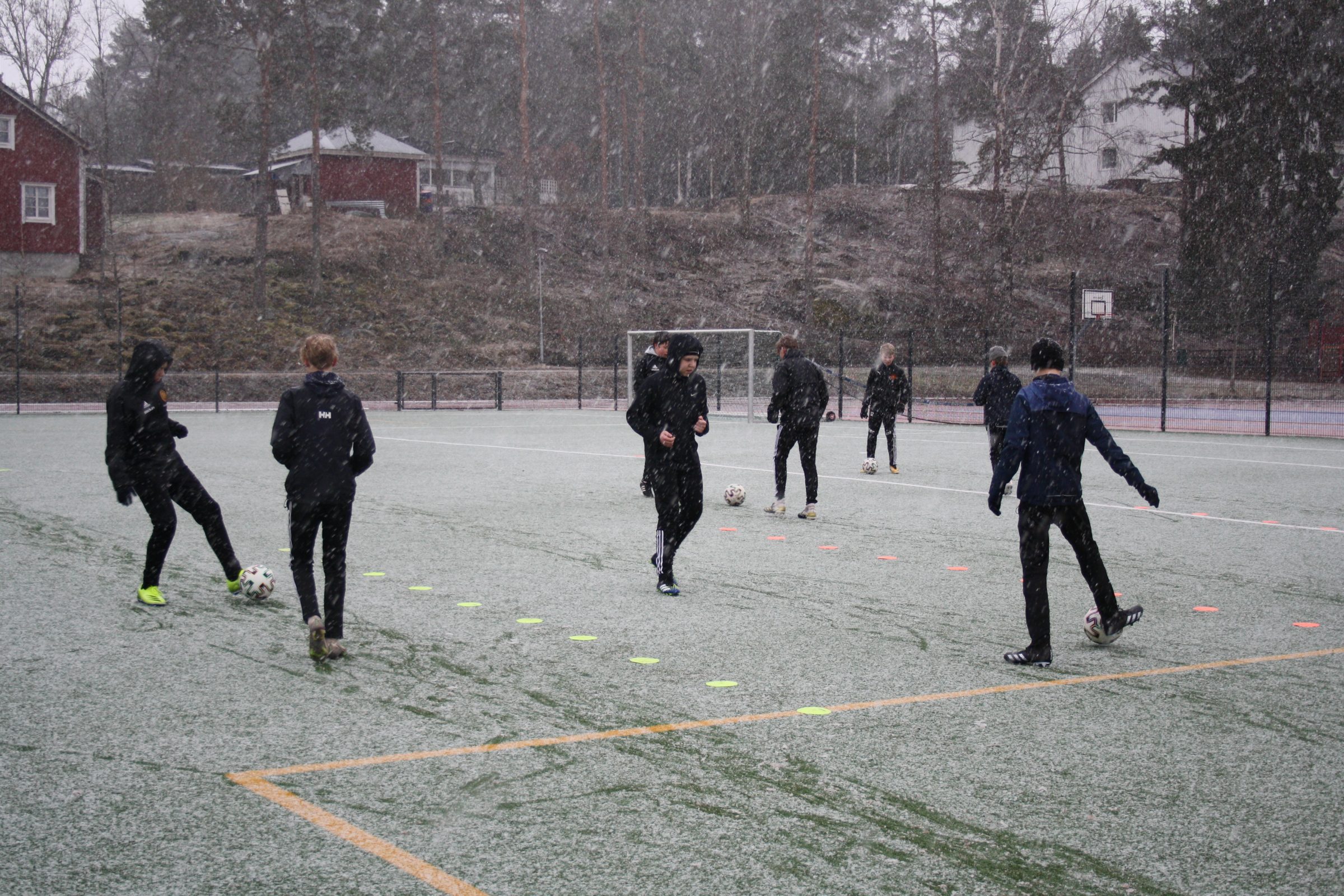 Fotbollslag som tränar i snöväder på fotbollsplan.