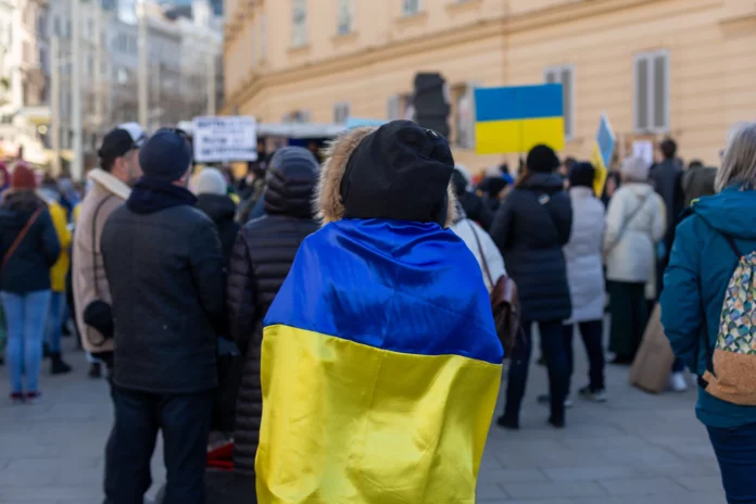 En bild på en grupp människor. I förgrunden står en person med en ukrainsk flagga svept kring sina axlar.