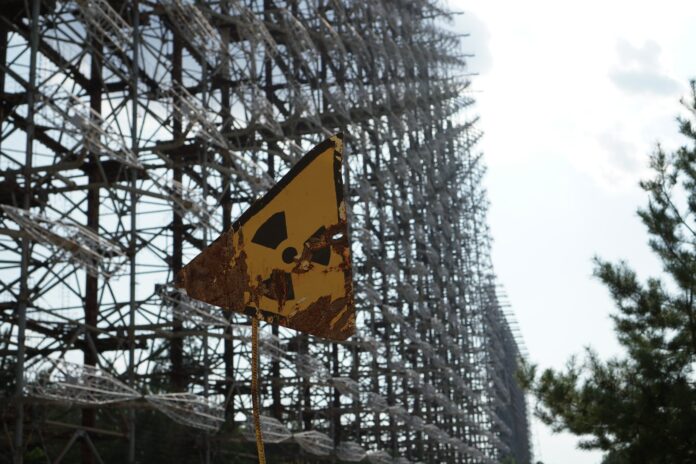 På bilden är en varningssymbol för radioaktivt avfall framför ett högt stängsel. Vädret är soligt.