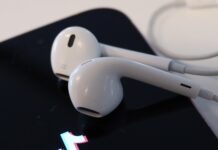 Artister och låtar från Universal återvänder till Tiktok Telefon med tiktok logon på skärmen. På telefonen ligger ett par vita hörlurar.