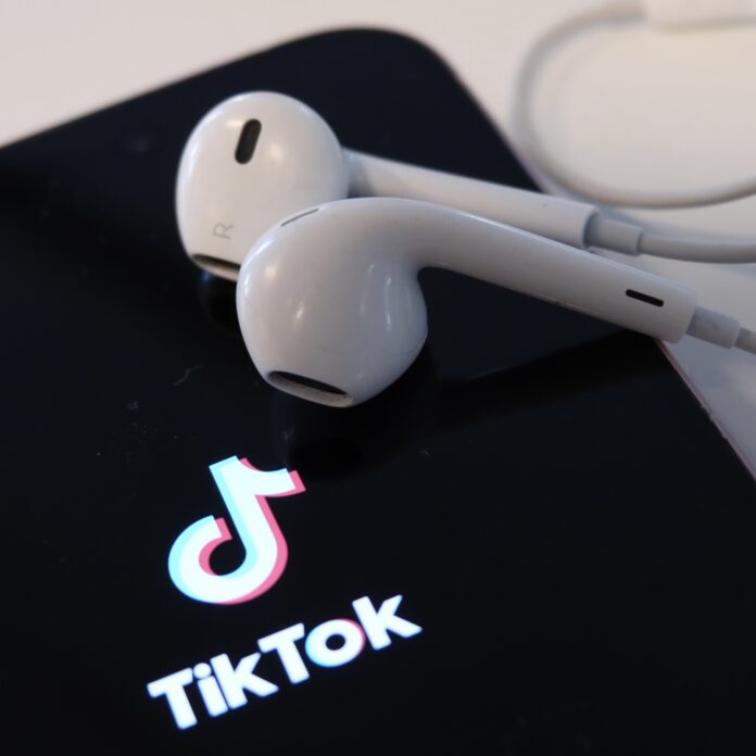 Telefon med tiktok logon på skärmen. På telefonen ligger ett par vita hörlurar.